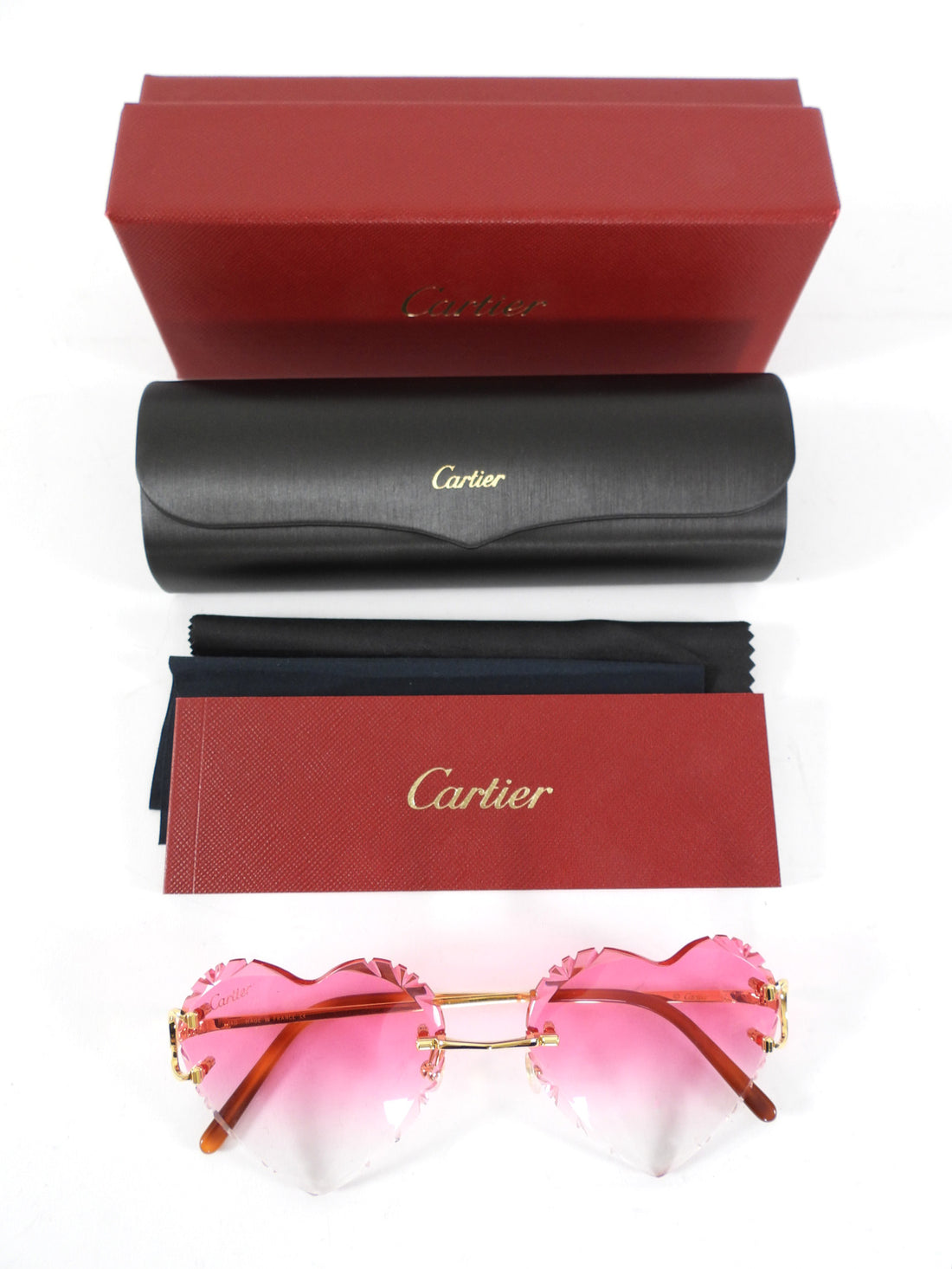 Cartier sunglasses with pink lenses and heart shape, accompanied by a black case and red box on a white background.