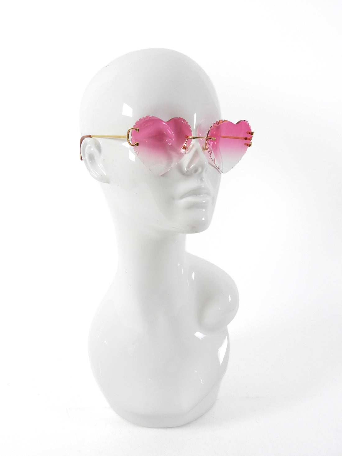 Sunglasses with pink heart-shaped lenses on a mannequin head against a white background