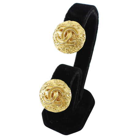 Gold Chanel earrings on a black stand with a white background