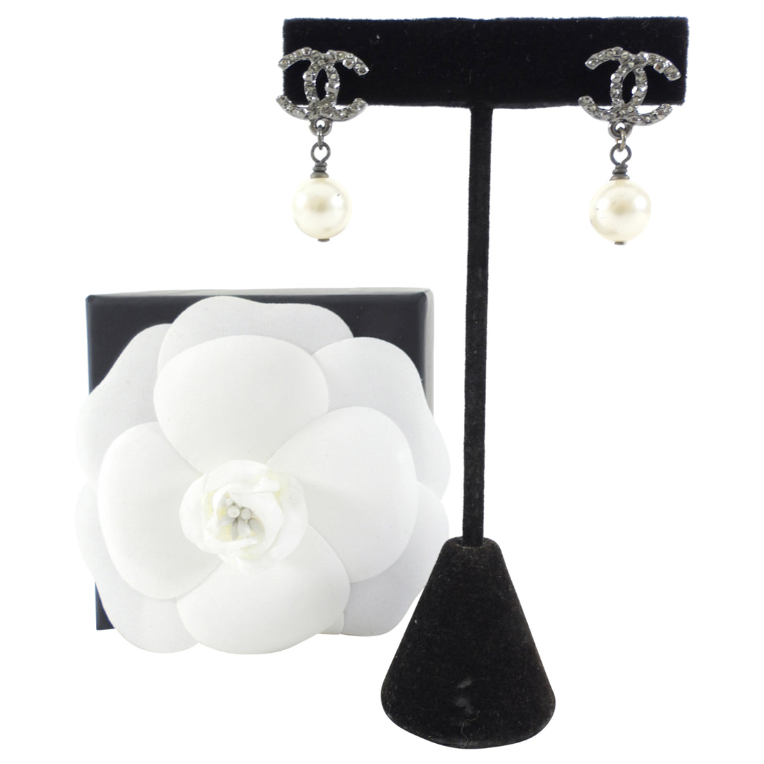 Chanel earrings on a black stand with a white flower display