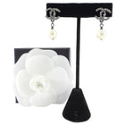 Chanel earrings on a black stand with a white flower display