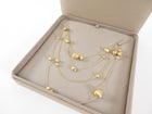 Gold necklace with spherical pendants in a beige jewelry box on a white background