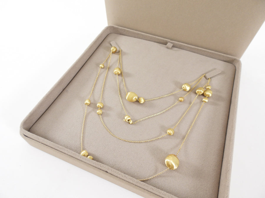 Gold necklace with spherical pendants in a beige jewelry box on a white background