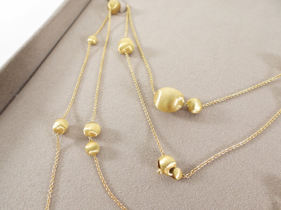 Two gold necklaces with beaded design on a gray surface