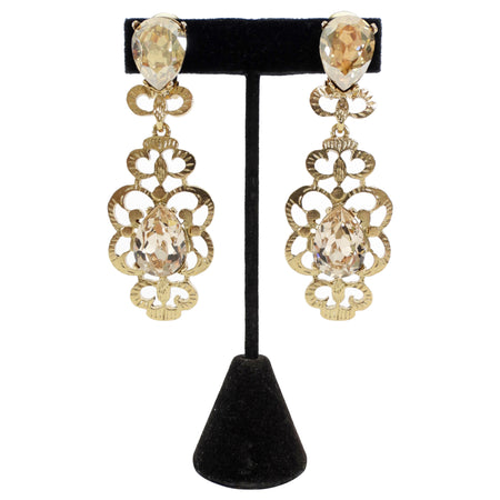 Gold earrings with clear gemstones on a black stand against a white background