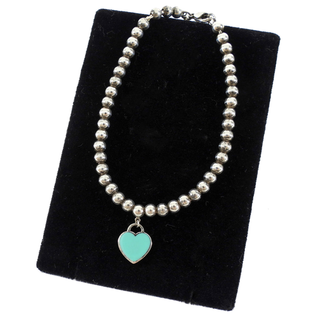 Tiffany & Co. Silver beaded necklace with a turquoise heart charm on a black velvet stand.