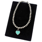 Tiffany & Co. Silver beaded necklace with a turquoise heart charm on a black velvet stand.