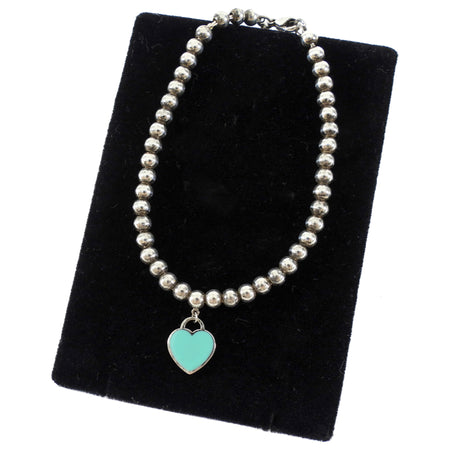 Tiffany & Co. Silver beaded necklace with a turquoise heart charm on a black velvet stand.