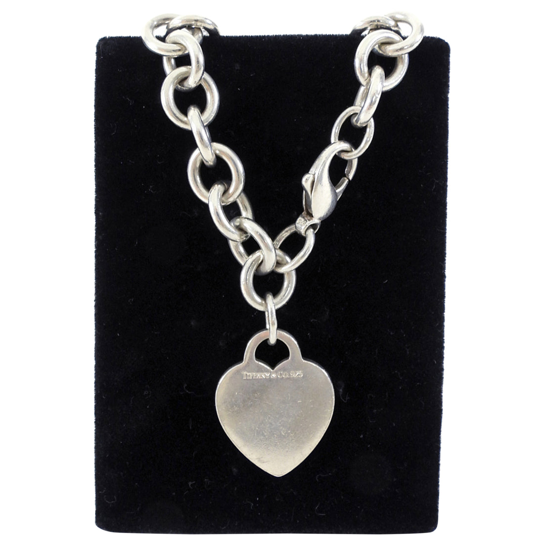 Tiffany & Co. Silver chain bracelet with a heart-shaped pendant on a black velvet stand.