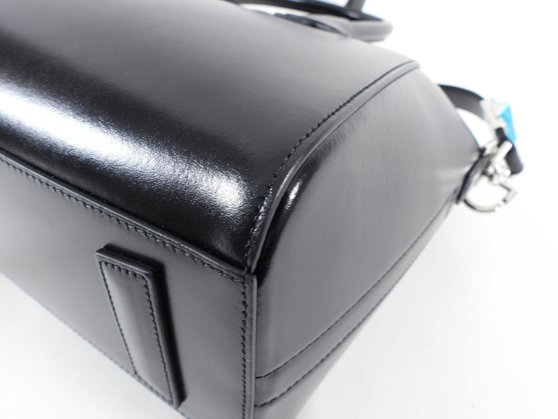 Structured buffed calfskin top handle bag in black. Twin rolled carry handles at top. Detachable shoulder strap with logo-engraved tab-slot fastening. Logo plaque at face. Leather bumper tabs at base. Zip closure at main compartment. Leather logo patch, zippered pocket, and patch pockets at interior. Tonal textile lining. Silver-tone hardware. Approx. 11" length x 9.75" height x 7" width.