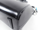 Structured buffed calfskin top handle bag in black. Twin rolled carry handles at top. Detachable shoulder strap with logo-engraved tab-slot fastening. Logo plaque at face. Leather bumper tabs at base. Zip closure at main compartment. Leather logo patch, zippered pocket, and patch pockets at interior. Tonal textile lining. Silver-tone hardware. Approx. 11
